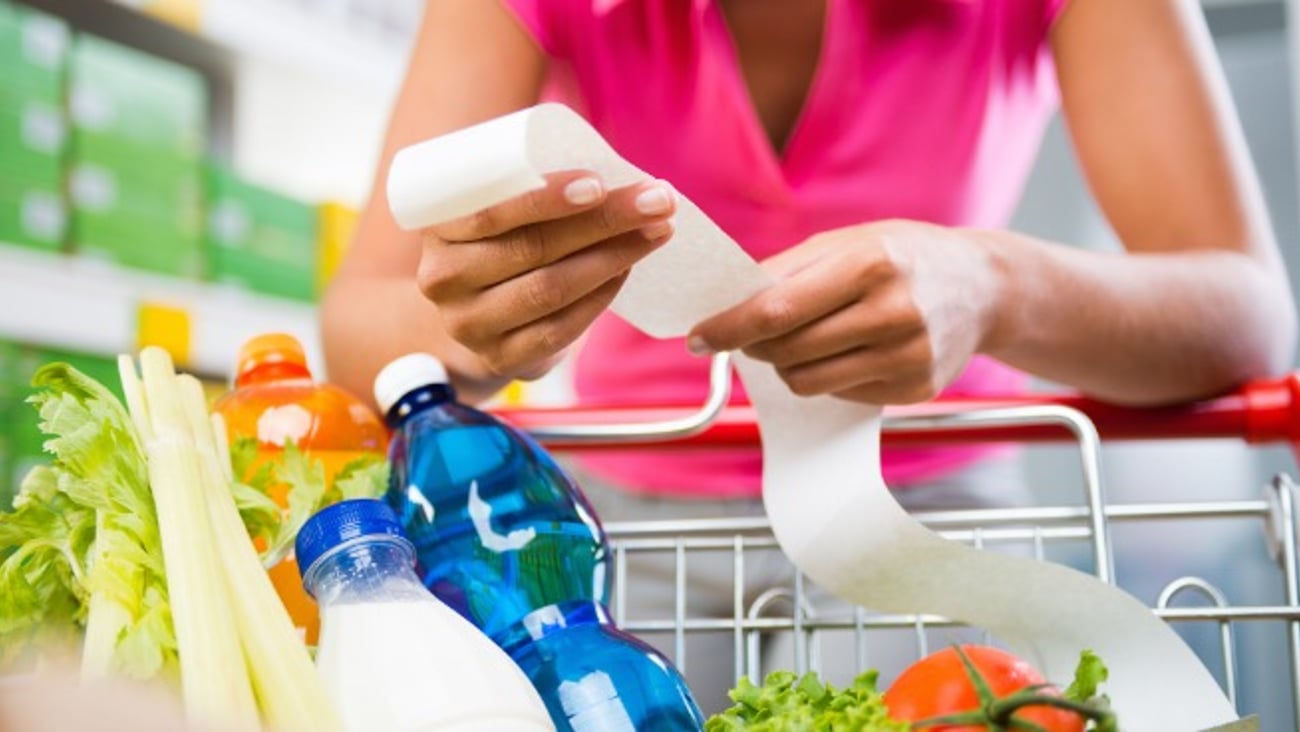 A woman leaning on her shopping cart full of groceries with a bill in her hand