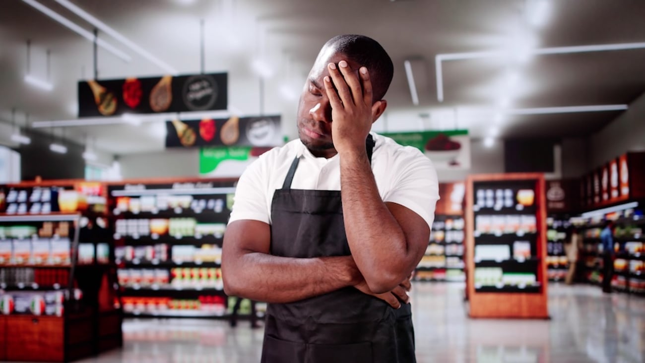 Employee stands in a grocery store with his hand on his face