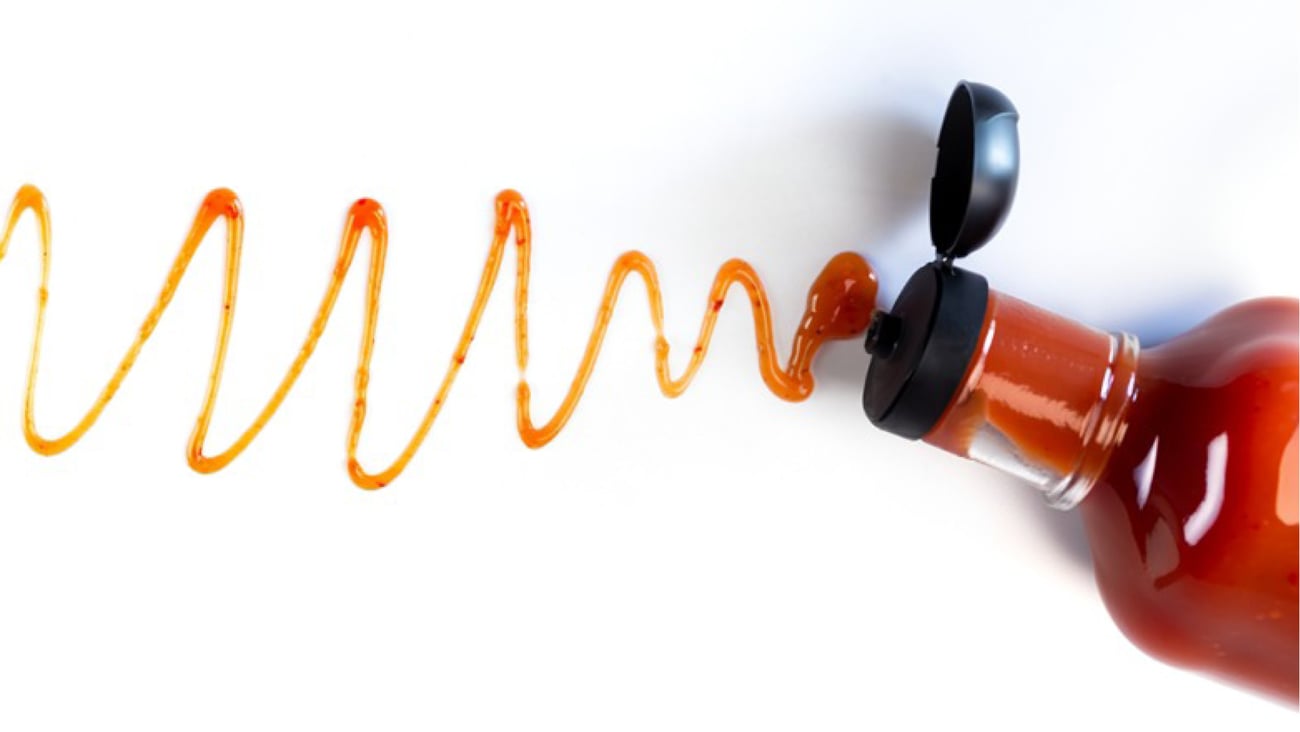 A bottle of red sauce in a glass bottle with a streak of sauce on a white background
