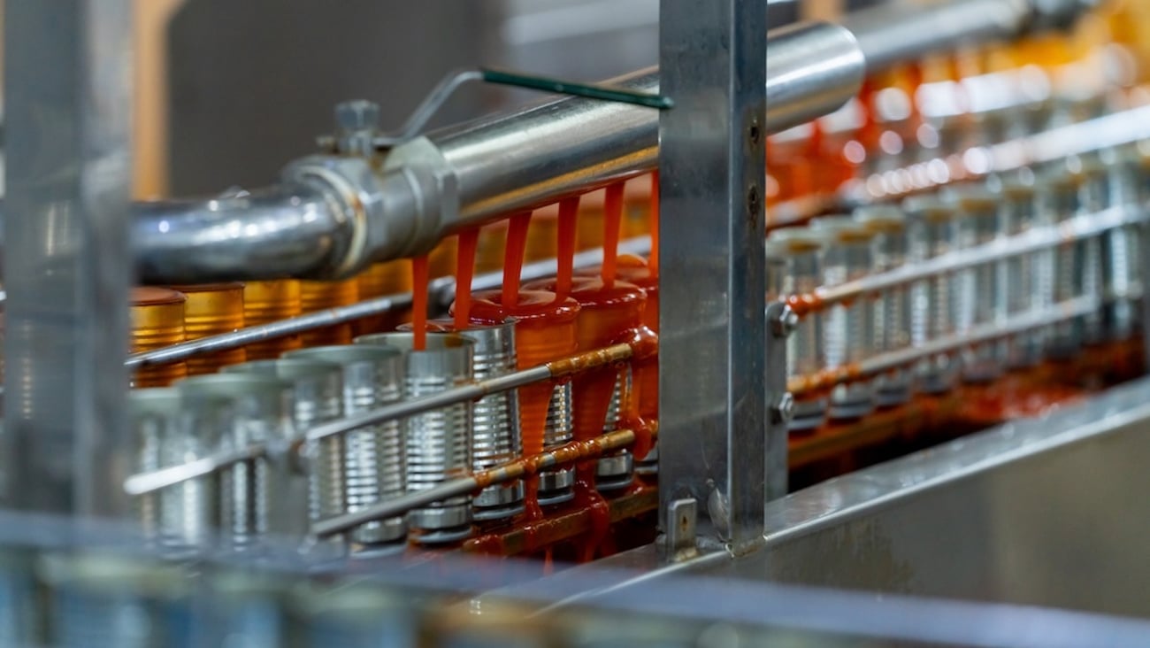 Cans on a manufacturing line getting filled with a red sauce.