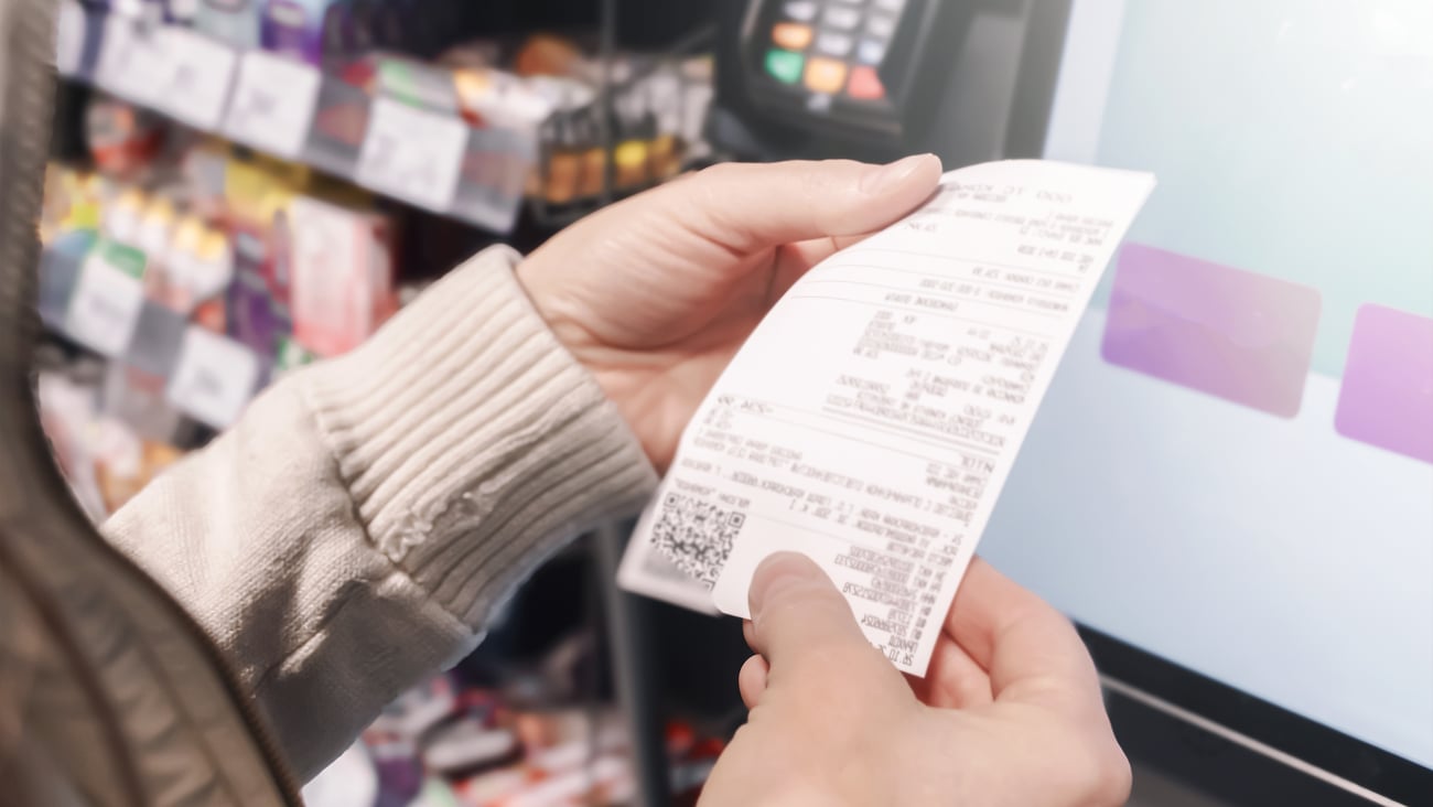 In a grocery store, a woman examines her receipt at a self-service checkout. She focuses on managing her family budget and tracking shopping expenses efficiently