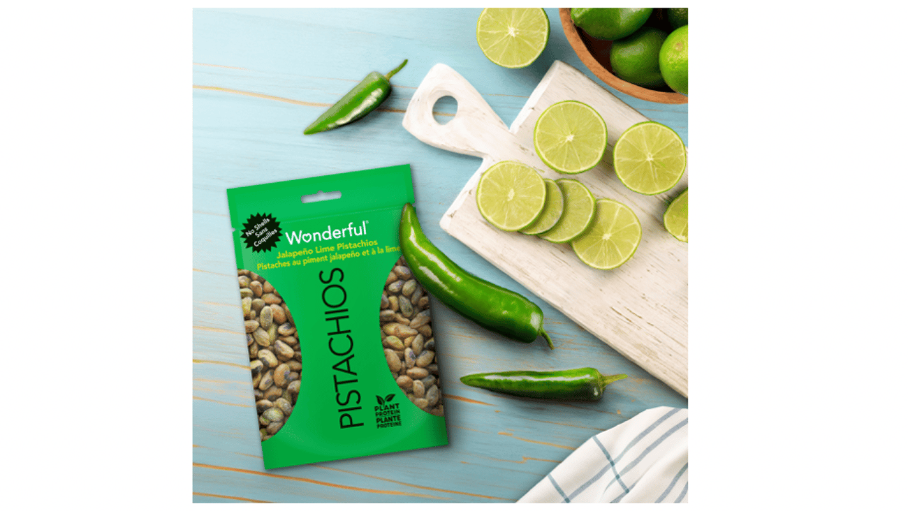 A bag of Wonderful Pistachios No Shells Jalapeño Lime on a blue table next to a cutting board with lime slices and jalapanoes
