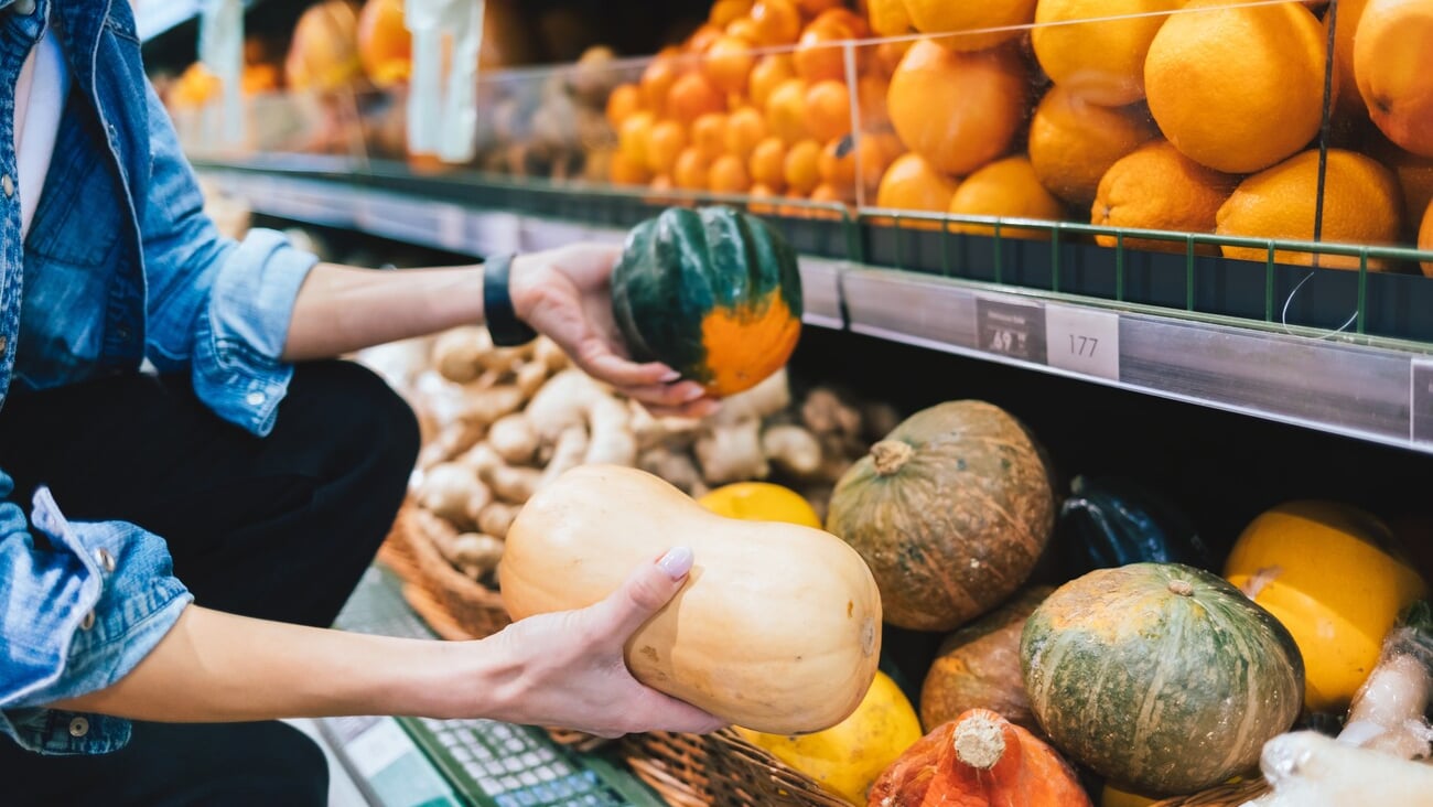 Unrecognizable girl choosing pumpkin in supermarket near shelf with organic fruits and vegetables, close-up; Shutterstock ID 2163652135