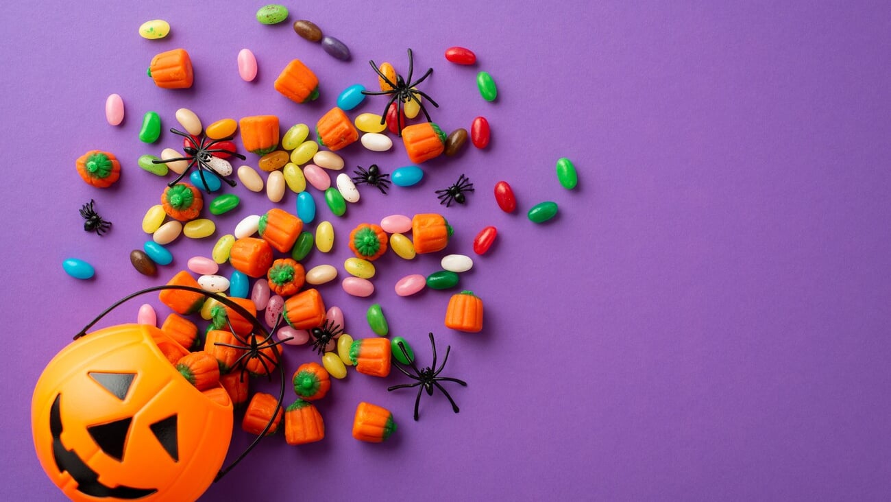 Top view photo of halloween decorations pumpkin basket with candies and spiders on isolated violet background; Shutterstock ID 2191379013