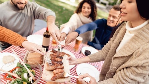 A group of young people gather around a picnic table for some BBQ picnic