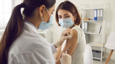 Woman in medical face mask getting Covid-19 or flu vaccine at the hospital. Professional nurse or doctor giving antiviral injection to patient