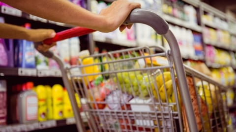 A female pushing a shopping cart down a grocery store aisle