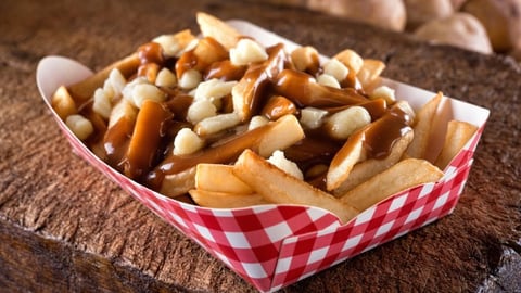 A serving of delicious poutine with french fries, cheese curds and gravy on a rustic wooden board