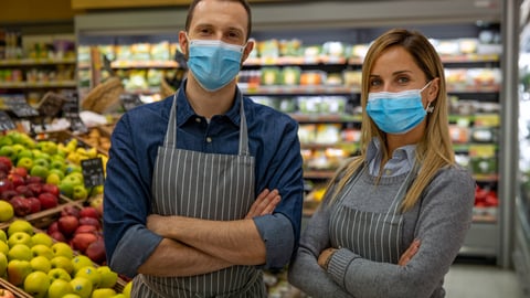 Staff workers wearing medical masks are looking in camera satisfied with their work in organic section at supermarket.