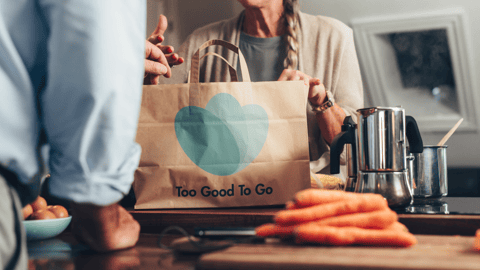 A man and woman standing in a kitchen unpacking a Too Good To Go paper bag