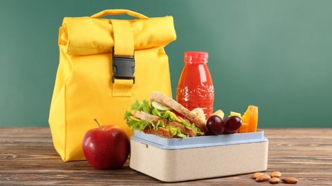 Lunch box with appetizing food and bag on wooden table against chalkboard background