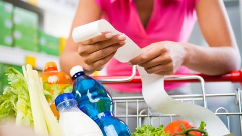 Woman checking a long grocery receipt leaning to a full shopping cart at store.