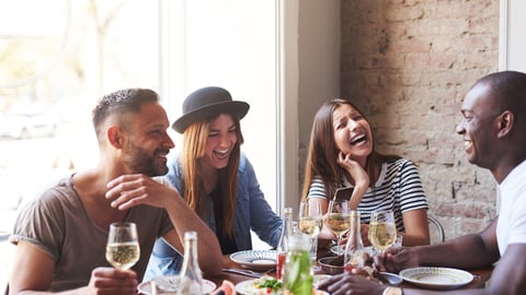 Group of young friends having fun and laughing while dining at table in restaurant.