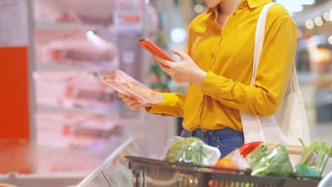 close up of asian young businesswoman is shopping for meat and scanning barcode with smart phone at supermarket