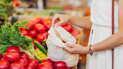 Female hands puts fruits and vegetables in cotton produce bag at food market.