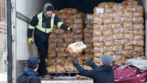 A man standing in the back of a truck passing out bags of potatoes