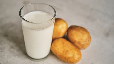 A glass of milk next to three potatoes