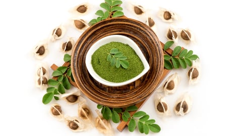Powdered moringa in a wooden bowl surrounded by leaves