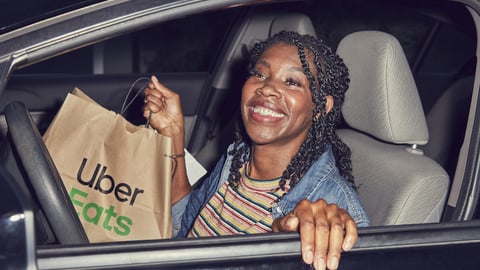 Female Uber driver holding an Uber Eats bag as she gets out of her car