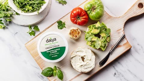 Daiya brand cream cheeze spread on a wooden board next to a bagel