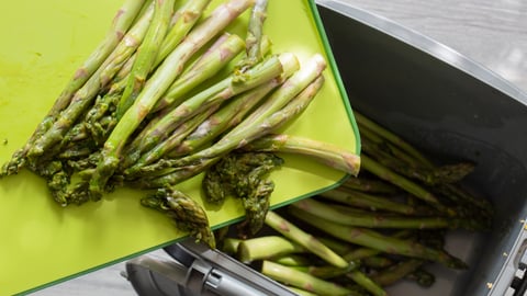 Rotten asparagus spears being thrown away into food waste recycling bin. Food waste concept