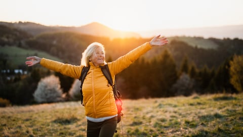 Front view of senior woman hiker standing outdoors in nature at sunset.