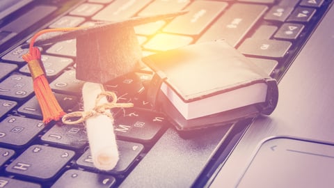 Graduation cap, diploma and text book sitting on top of a laptop keyboard