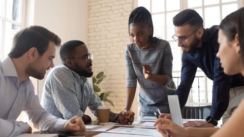 Serious multiracial corporate business team and black leader talk during group briefing, focused diverse colleagues brainstorm discuss report paperwork engaged in teamwork at meeting gather at table