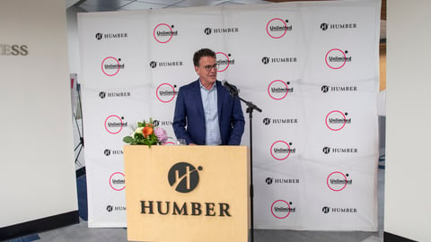 Anthony Longo standing at a podium in front of a Humber College branded step and repeat