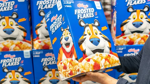 Customer hand holding a family size package of Kellogg's brand Frosted Flakes cereal in a supermarket aisle