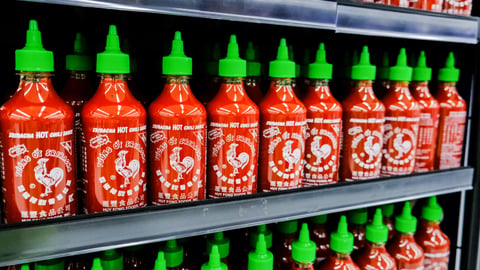 Plastic bottles of Huy Fong Food Sriracha hot chili sauce in a supermarket aisle