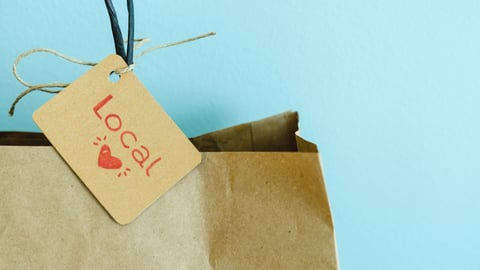 Paper shopping bag with label on blue background. Label with heart and text LOCAL. Shopping concept