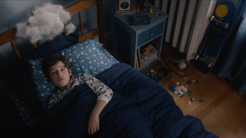 Young boy lying in bed with a cloud over his head