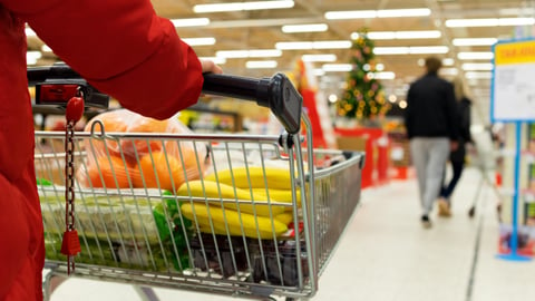 woman pushing grocery cart with food and christmas tree in background