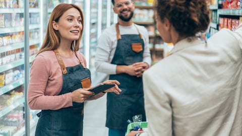 Two grocery store workers talking to a customer 