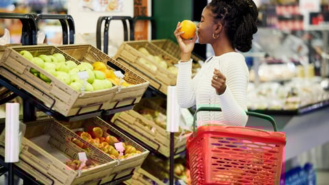 woman smelling an orange at the grocery store