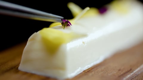 A stick of lab-grown butter with tweezers placing a flower on top