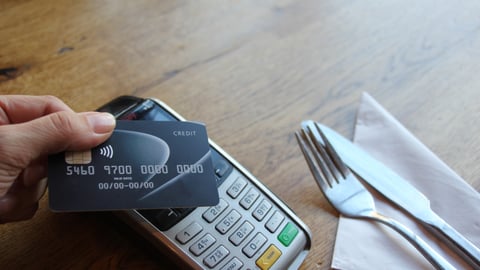 A hand holding a debit card and tapping in on the payment terminal