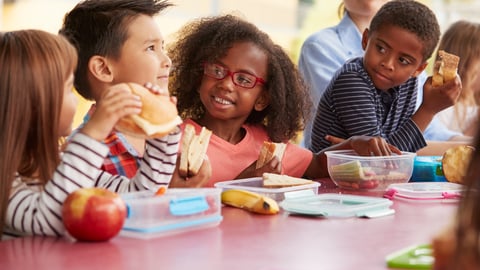 Young school kids eating lunch talking at a table together