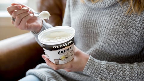 A woman sitting eating out of a tub of OIympic Organic yogurt