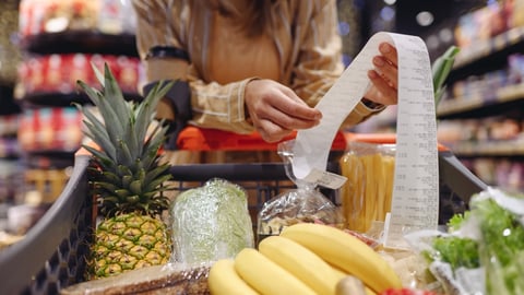 Woman looks at a grocery bill above a shopping cart of produce