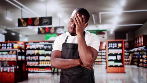 Employee stands in a grocery store with his hand on his face