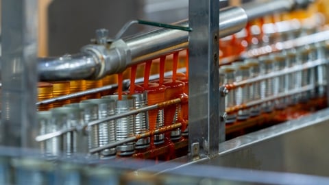 Cans on a manufacturing line getting filled with a red sauce.