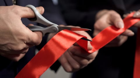 close up of ribbon cutting hand holding scissors and holding ribbon