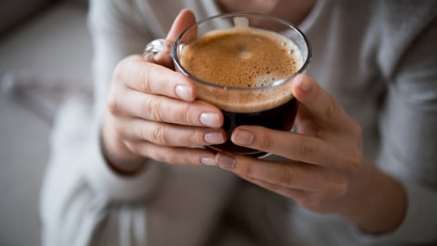 Two hands holding a cup of black coffee in a clear mug