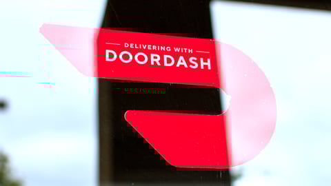 Close up. A red sticker decal on a restaurant door advertising delivery service available through DoorDash on-demand prepared food delivery service