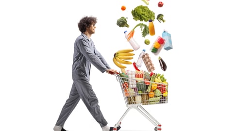 Man in pajamas pushing a shopping cart with falling groceries isolated on white background