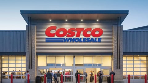 Outside shot of a Costco at night with people in the entrance way