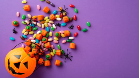 Top view photo of halloween decorations pumpkin basket with candies and spiders on isolated violet background; Shutterstock ID 2191379013