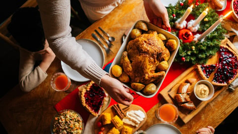 Close-up top view of young father male putting dish with baked hot turkey on holiday dinner table served for Christmas family party, celebrating thanksgiving day with roasted turkey for dinner.; Shutterstock ID 2226983789